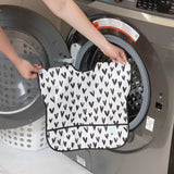 Someone puts a Bumkins Junior Bib: Hearts, which is waterproof and features black and white hearts, into a front-loading washer.