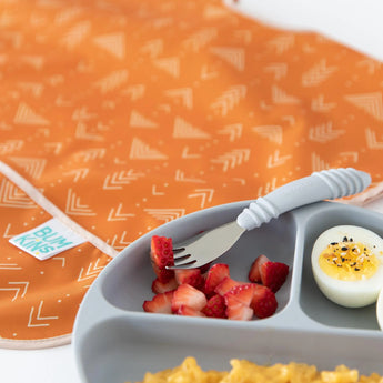 Close-up of a gray plate with strawberries and eggs, a gray fork, and Bumkins Junior Bib: Grounded on a white background.