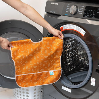 A person holds a Bumkins Junior Bib: Grounded in front of an open washing machine.