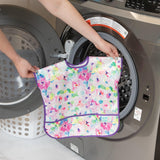 A person puts a Bumkins Junior Bib: Watercolor into a front-loader for easy cleaning; its waterproof and colorful.