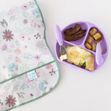 Bumkins Grip Dish Essential Toddler 4-Piece Mealtime Set: Lavender with breakfast foods sits next to a floral bib on a white background.