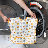 A person holds Bumkins Junior Bib: Winnie and Friends in front of an open front-loading washing machine.