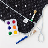 Close-up of a Bumkins Short-Sleeved Smock: Mickey Mouse Icon B+W on a white background, with a paint palette and paintbrushes nearby.