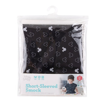 Bumkins Short-Sleeved Smock: Mickey Mouse Icon B+W is shown folded in a plastic packaging bag with a hanger and cardboard insert.