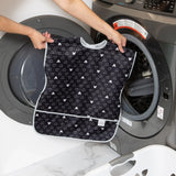 A person holds a Bumkins Short-Sleeved Smock: Mickey Mouse Icon B+W in front of an open front-loading washing machine.
