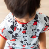 A child wearing a Bumkins Short-Sleeved Smock: Mickey Mouse Classic looking down.