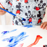 Close-up of a child painting in blue, wearing a Bumkins Short-Sleeved Smock: Mickey Mouse Classic.