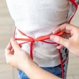 Close-up of hands tying the adjustable ribbon closure of a Bumkins Short-Sleeved Smock: Mickey Mouse Classic around a child's waist.