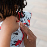 Close-up of hands fastening the hook-and-loop closure of a Bumkins Short-Sleeved Smock: Mickey Mouse Classic on a child.
