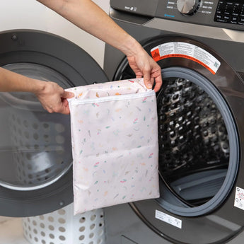 A person holds Bumkins Wet Bag: Princess Magic in front of an open front-loading washing machine.