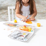 A child enjoys modeling clay and art supplies at a white table with Bumkins Clear Travel Bag 3-Pack: Wander.