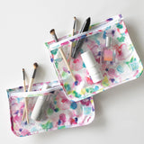 Two Bumkins floral makeup pouches from the Clear Travel Bag 3-Pack: Watercolor, featuring TSA compliant items on a white surface.