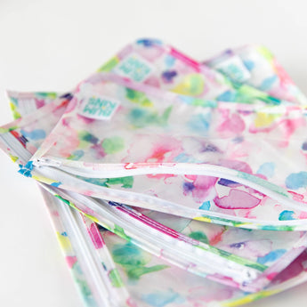 Three TSA compliant, waterproof Clear Travel Bag 3-Pack: Watercolor by Bumkins on a white surface.
