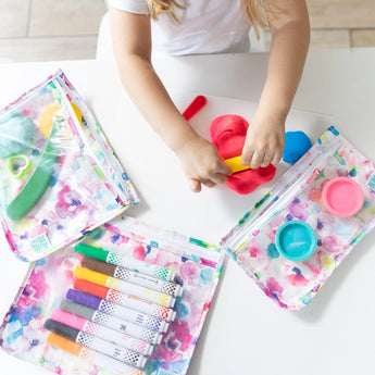 A child plays with colorful dough and tools on a table, surrounded by art supplies in Bumkins watercolor Clear Travel Bag 3-Pack.