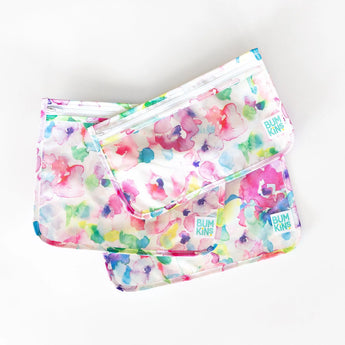 Three Bumkins Clear Travel Bags in watercolor patterns fan out on a light background, highlighting their vibrant, waterproof design.