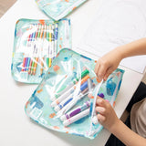 A child organizes colorful markers in a Bumkins ocean-themed pouch from the Clear Travel Bag 3-Pack, with a drawing sheet nearby.