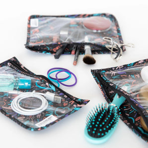 Assorted beauty tools, makeup, and hair ties organized in Bumkins Clear Travel Bag 3-Pack: Channel Kindness on a white background.