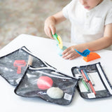 A child plays with modeling clay at a table, surrounded by Bumkins Clear Travel Bag 3-Pack: Mickey Mouse Icon Black + White. These pouches feature a black pattern and white zippers, containing extra clay, tools, and pens against a softly blended background.