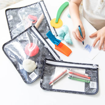 Child drawing with tools and playdough, next to Bumkins 3-Pack Clear Travel Bags: Mickey Mouse Icon Black + White with craft items.