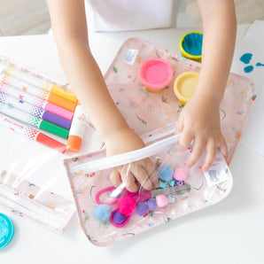 A child organizes craft supplies in bags from Bumkins The Chaos Coordinator Essential 4-Piece Set: Disney Princess Magic on a white table.