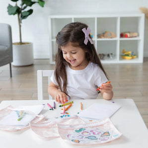 A young girl colors with crayons at a white table while Bumkins Clear Travel Bag 3-Pack: Lace lays nearby.